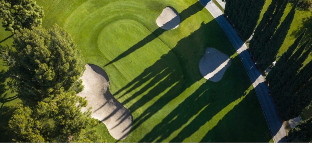Drone view of a golf green with two sand bunkers and long tree shadows at San Dimas Canyon Golf Course