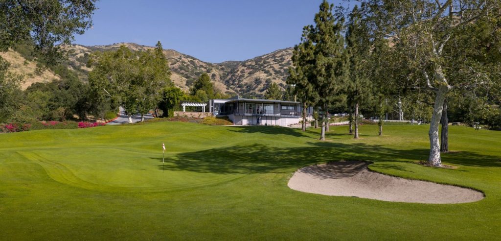 Golf green with sand bunker in front of the clubhouse at San Dimas Canyon Golf Course, surrounded by mountains and pine trees